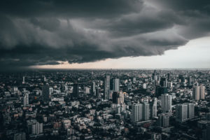 Luftaufnahme einer grauen Stadt, darüber dunkelgraue Wolken