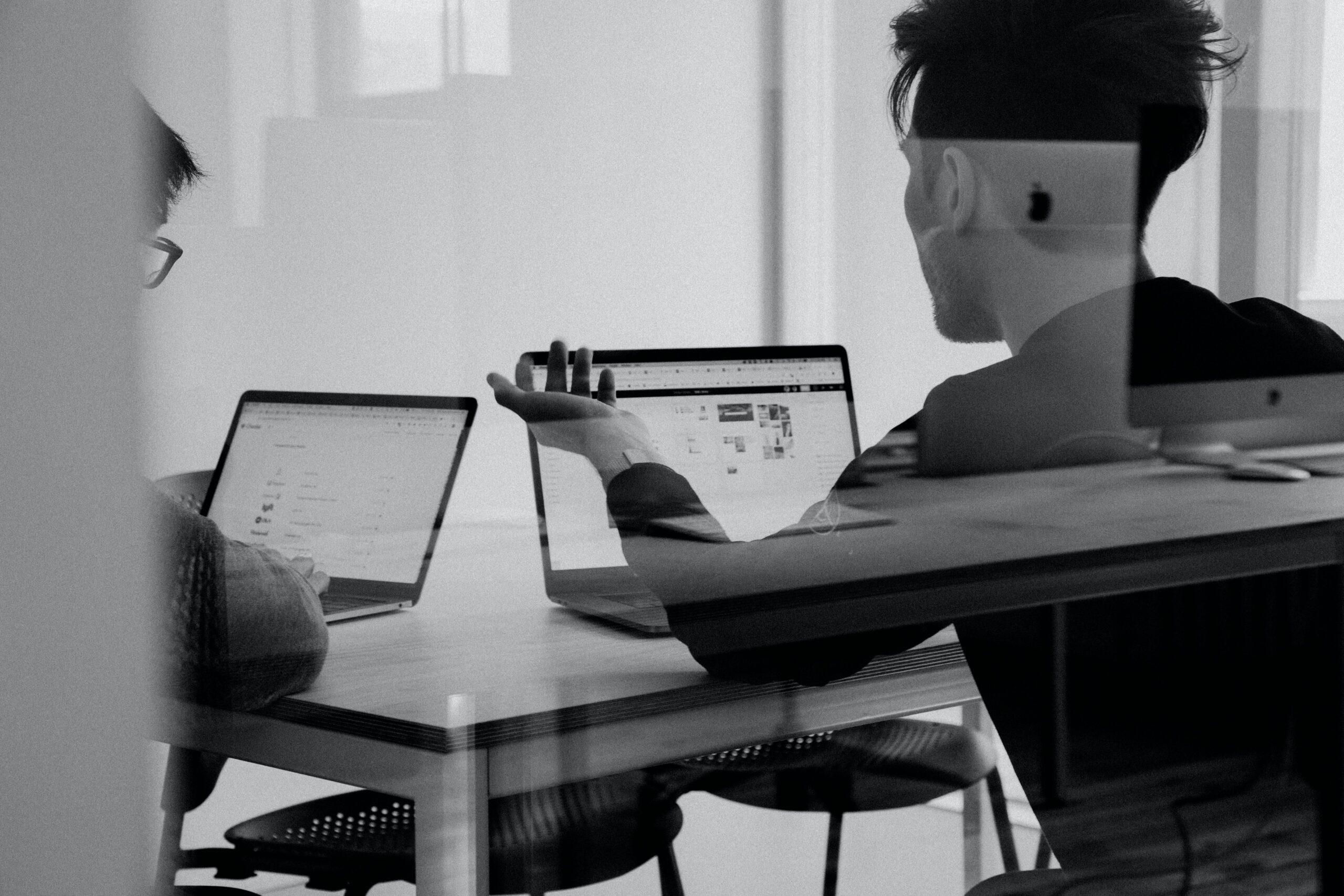 zwei Mitarbeiter (von hinten) sitzen vor Laptop, schwarz-weiß